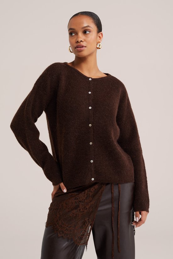Bruin gebreid vest met knopen, gedragen door een model met gouden oorbellen en een bruine leren broek met kanten details.