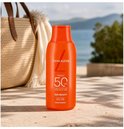 Lancaster Sun Beauty Body Milk SPF50 op een strand met een rieten tas op de achtergrond.
