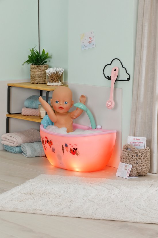 Pop met schuim in een roze, verlicht babybadje met douche, in een badkamer.