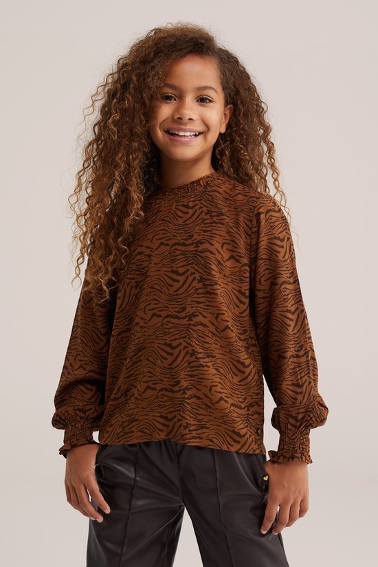 Meisje met krullen draagt een bruine blouse met tijgerprint en een zwarte broek.