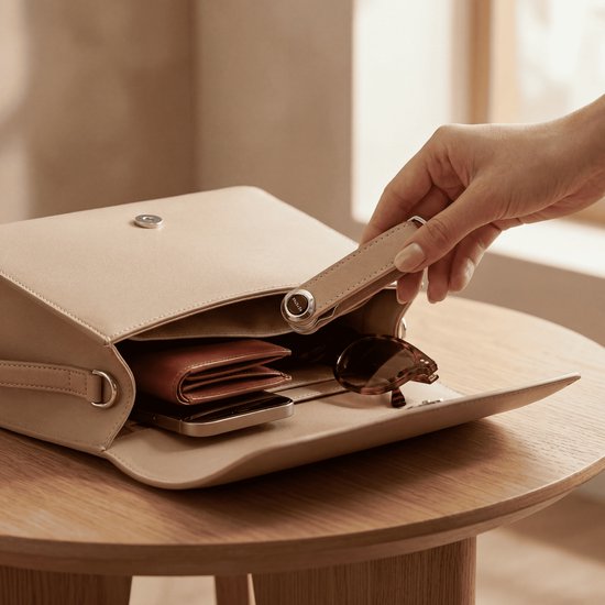 Hand opent beige tas met een bruine leren sleutelhanger en sleutels erin.