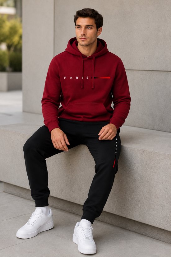 Man zittend in bordeauxrode hoodie met 'PARIS'-print en zwarte joggingbroek met 'PARIS'-print.