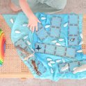 Kind speelt met blauwe magnetische Connetix tegels en dierenfiguren op een blauwe doek.