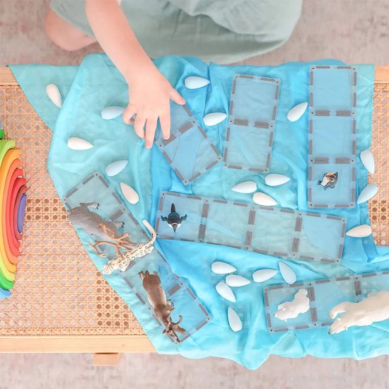 Kind speelt met blauwe magnetische Connetix tegels en dierenfiguren op een blauwe doek.