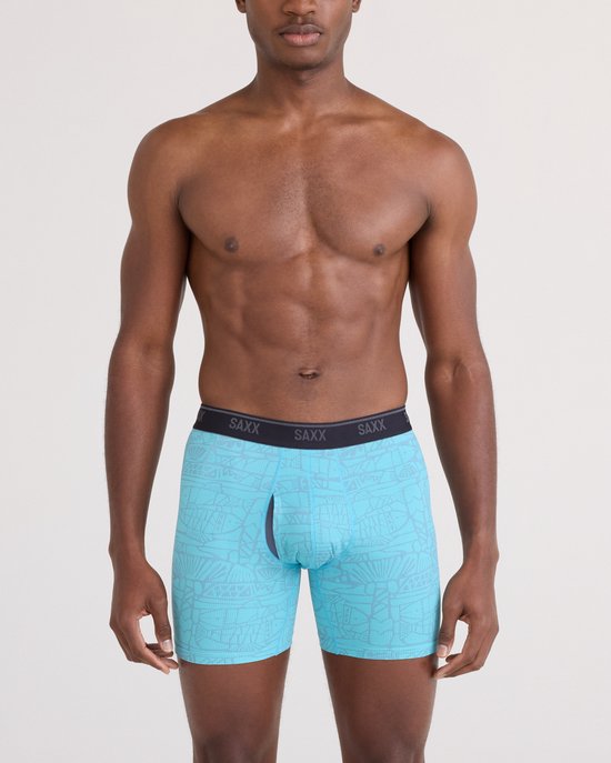 Man van voren gezien in lichtblauwe boxershort met grijze print, zwarte SAXX-band en opening.