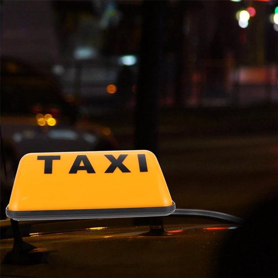 Oranje taxibord met zwarte letters 'TAXI' op een autodeel, 's nachts.