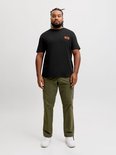 Model in zwart T-shirt met oranje label op de borst en legergroene cargo broek.