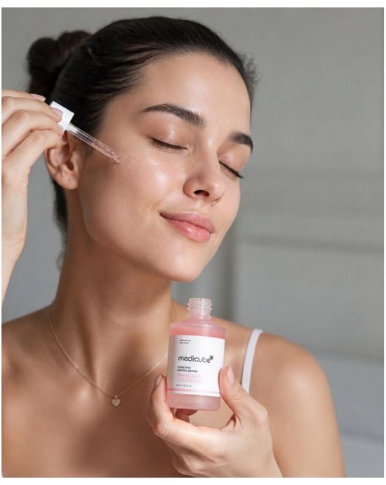 Een vrouw met donker haar brengt Medicube PDRN Pink Peptide Serum aan op haar gezicht.