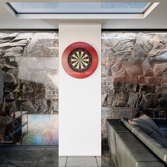 Rood dartbord met groen, zwart en wit op een witte muur in een kamer met stenen muur en zwarte bank.