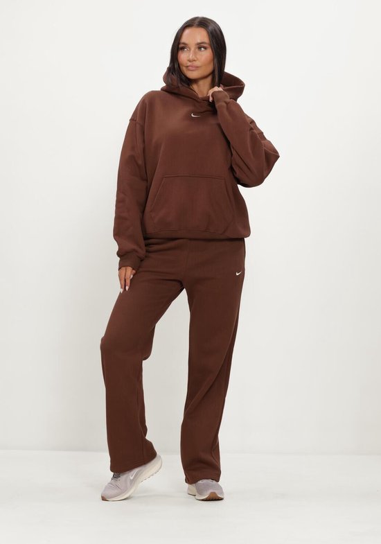 Model in bruine Nike joggingbroek en hoodie met kleine Nike logo's.