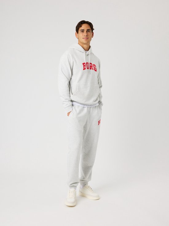 Man in lichtgrijze hoodie met rode 'BORG' letters op de borst, en bijpassende joggingbroek.