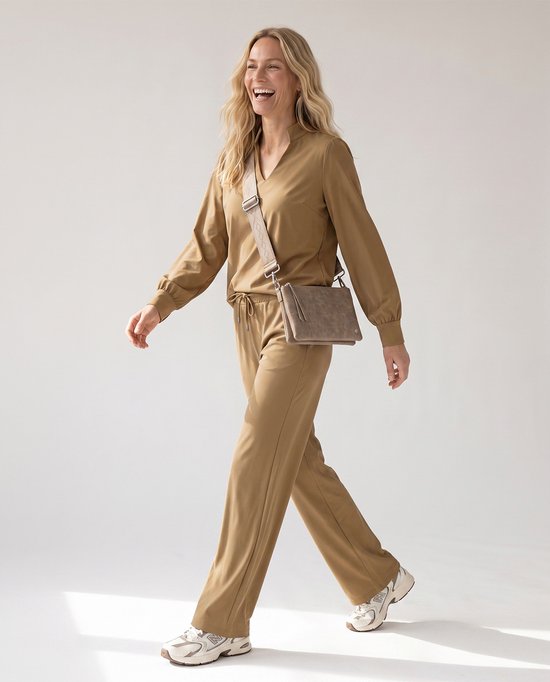 Model draagt een bruine travelstof broek met rechte pijpen, bijpassende blouse en crossbodytas.