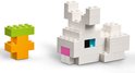 Een wit LEGO konijn met blauwe ogen, een roze neus en een groene en oranje wortel ernaast.