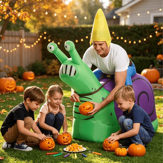 Een man in een opblaasbaar slakkenkostuum zit met drie kinderen in een tuin, die pompoenen uitsnijden.
