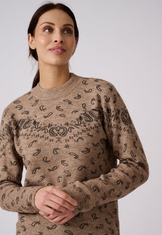 Close-up van het model in een beige trui met zwarte paisley-print en ronde hals, tegen een neutrale achtergrond.