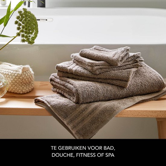 Pile de serviettes taupe avec détail côtelé sur un banc en bois près d'une baignoire.