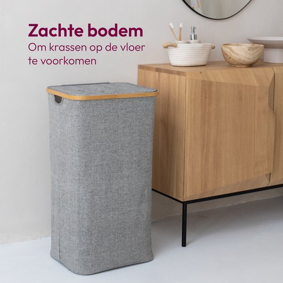 Grijze wasmand met bamboe deksel staat naast een houten kast met spiegel. Tekst: 'Zachte bodem om krassen op de vloer te voorkomen'.