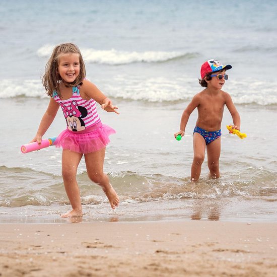 Meisje in roze gestreept badpak met tule rok en Minnie Mouse-print aan de waterkant.