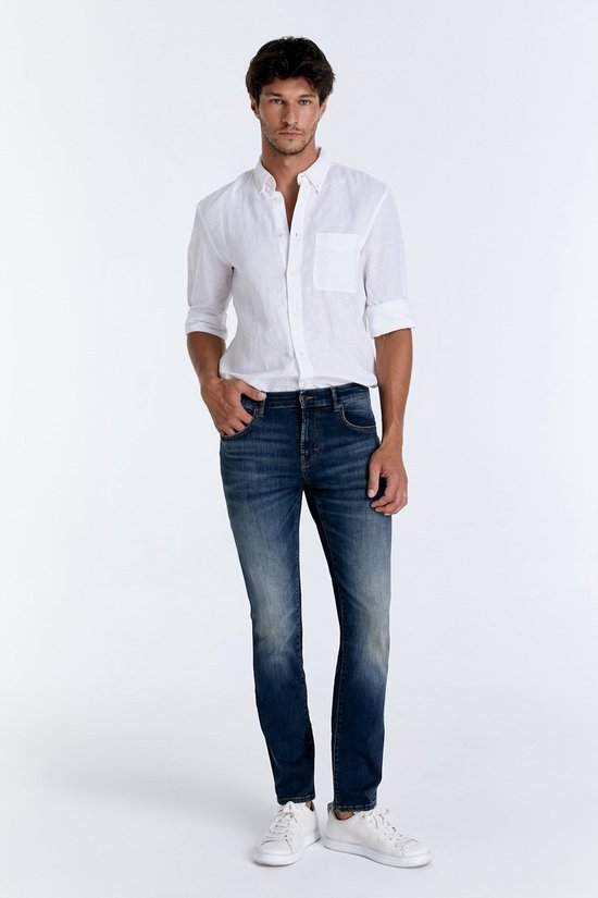 Man staand, dragend donkerblauwe straight-fit jeans, wit overhemd en witte sneakers.