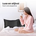 Een vrouw in een roze badjas drinkt thee op een bed met zwarte satijnen kussenslopen.