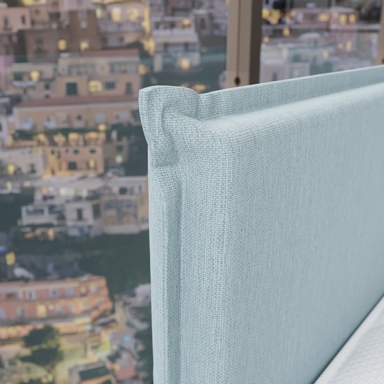 Lichtblauwe boxspringkop in detail, met zicht op een stad op een heuvel.