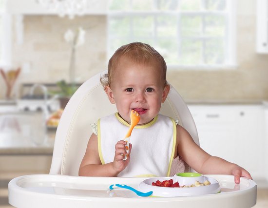 Bébé souriant dans une chaise haute avec bavoir, cuillère orange dans la bouche