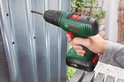 Hand met Bosch boormachine boort in een metalen plaat. Boormachine is groen en zwart met rode details.