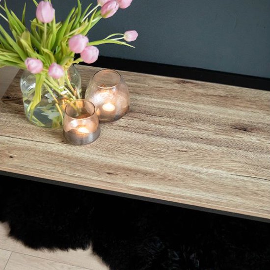 Salontafel met licht houten blad, zwart stalen frame. Een boeket roze tulpen en glazen windlichten met kaarsen. Zwart schapenvachtje eronder.