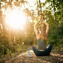 Vrouw in yoga houding in een bos bij zonsondergang, met kleine Boeddhabeeldje.