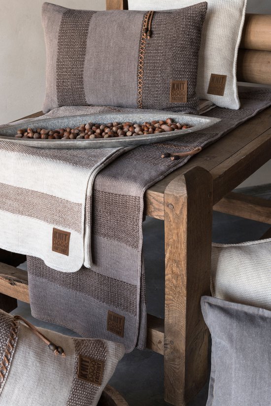 Bruine en grijze gestreepte kussens en plaid, gerangschikt op een houten tafel.