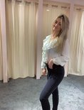 Een vrouw met blond haar in een witte blouse met ruches en een skinny jeans in donkergrijs.
