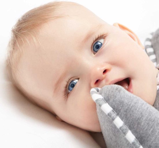 Close-up van een baby met blauwe ogen, die met de vingers in de grijze Swaddle UP slaapzak bijt.