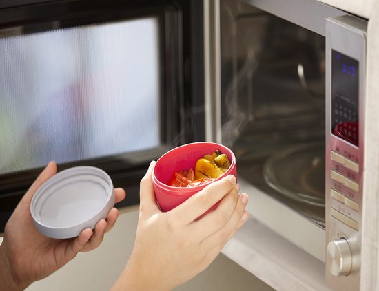Pot à collation rouge contenant des légumes cuits à la vapeur, retiré d'un four à micro-ondes.