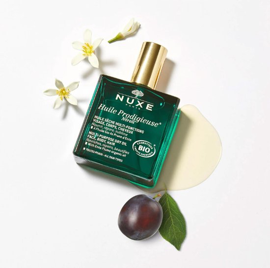 Groene Nuxe Huile Prodigieuse Néroli fles met gouden dop, met pruimen en witte bloesems.