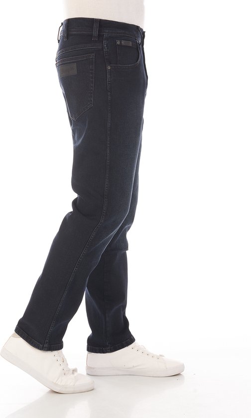 Zijaanzicht man in donkerblauwe straight fit jeans en witte sneakers.