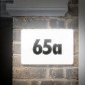 Verlicht huisnummer '65a' op een bakstenen muur.