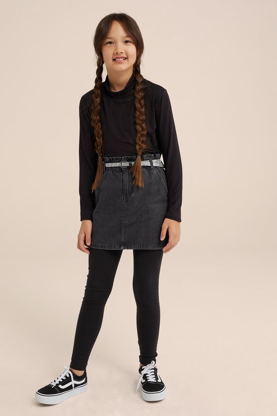 Meisje in een grijze denim rok met hoge taille, riem, coltrui en zwarte legging.