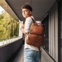 Leren rugzak in cognac kleur gedragen door een man in een wit hemd en spijkerbroek.