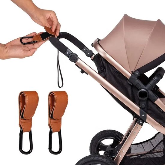 Een hand die een bruine kinderwagenhaak aan een kinderwagenhandvat bevestigt. Twee haken liggen onderaan.