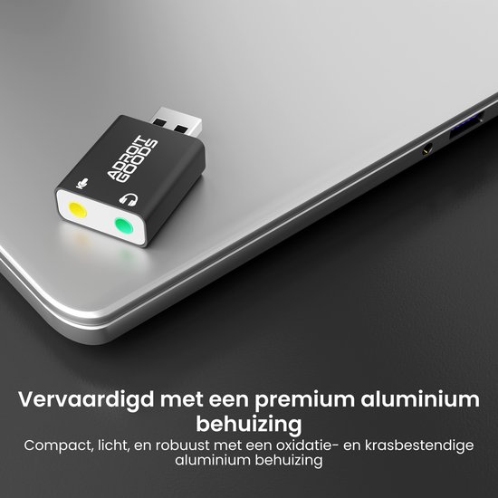 Zwarte USB-geluidskaartadapter op een laptop, met microfoon- en hoofdtelefoonaansluitingen.