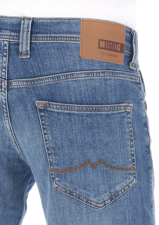 Close-up van de achterkant van een blauwe jeans met het Mustang 'True Denim' label. De achterzakken hebben stiksels.