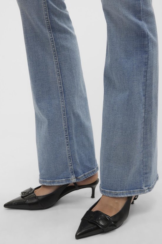 Gros plan sur le bas d'un jean flare bleu clair avec surpiqûres blanches et chaussures noires à boucle.