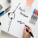 Een hand schrijft "Alex's Notebook KEEP OUT!!" met een zwarte Sharpie marker in een notitieboek. Kleurrijke markers liggen ernaast.