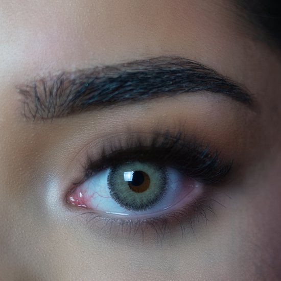 Close-up van een oog met een grijsgroene contactlens en bruin in het midden. Wenkbrauw is donker.