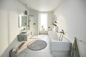 Lichte badkamer met ligbad, douche, wastafel en een matzwarte toiletrolhouder bij de toiletruimte.