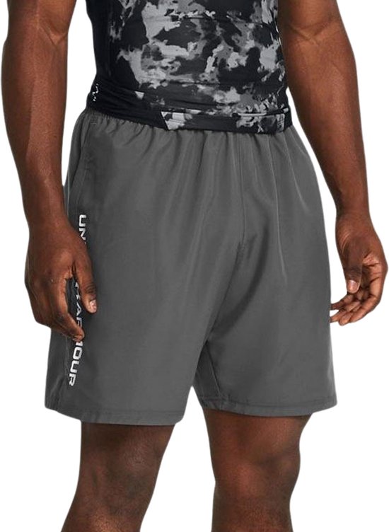 Grijze sportbroek van Under Armour met witte tekst op de zijkant, gedragen door een man.