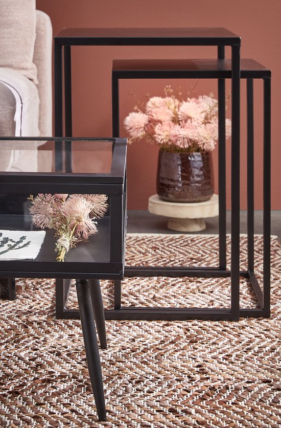 Zwarte metalen bijzettafels met een glazen displaykastje en bloemen.