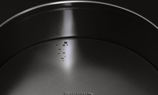Zwarte metalen springvorm met een licht gebogen rand en waterdruppels.