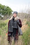 Model in grijze gebreide sjaal, muts en handschoenen. Draagt een bordeauxrode vest en zwarte jurk.
