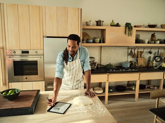 Man met een schort die naar een e-reader kijkt die op een met bloem bestoven tafel ligt.